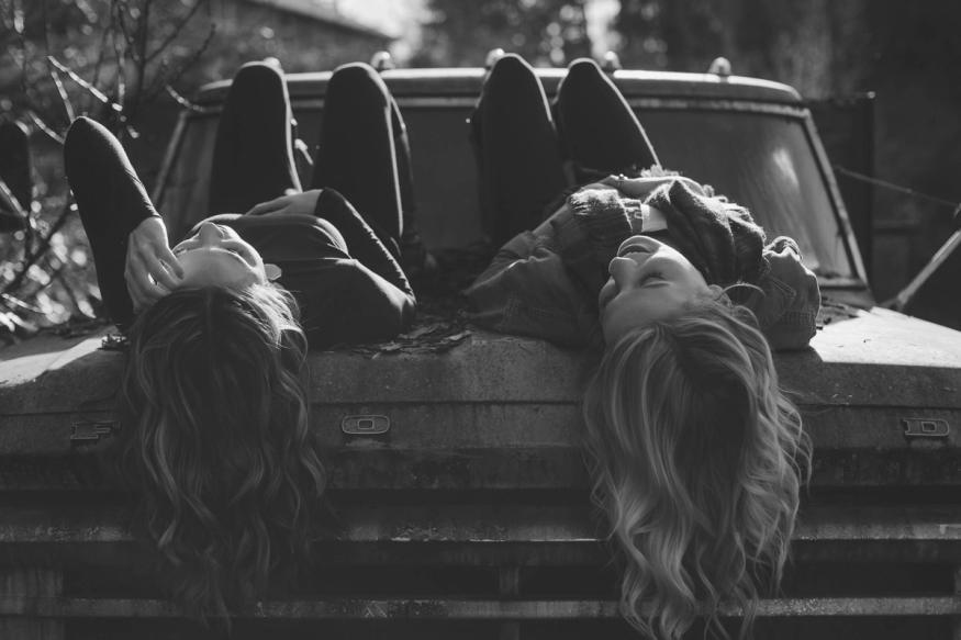 two girls laying on old car talking