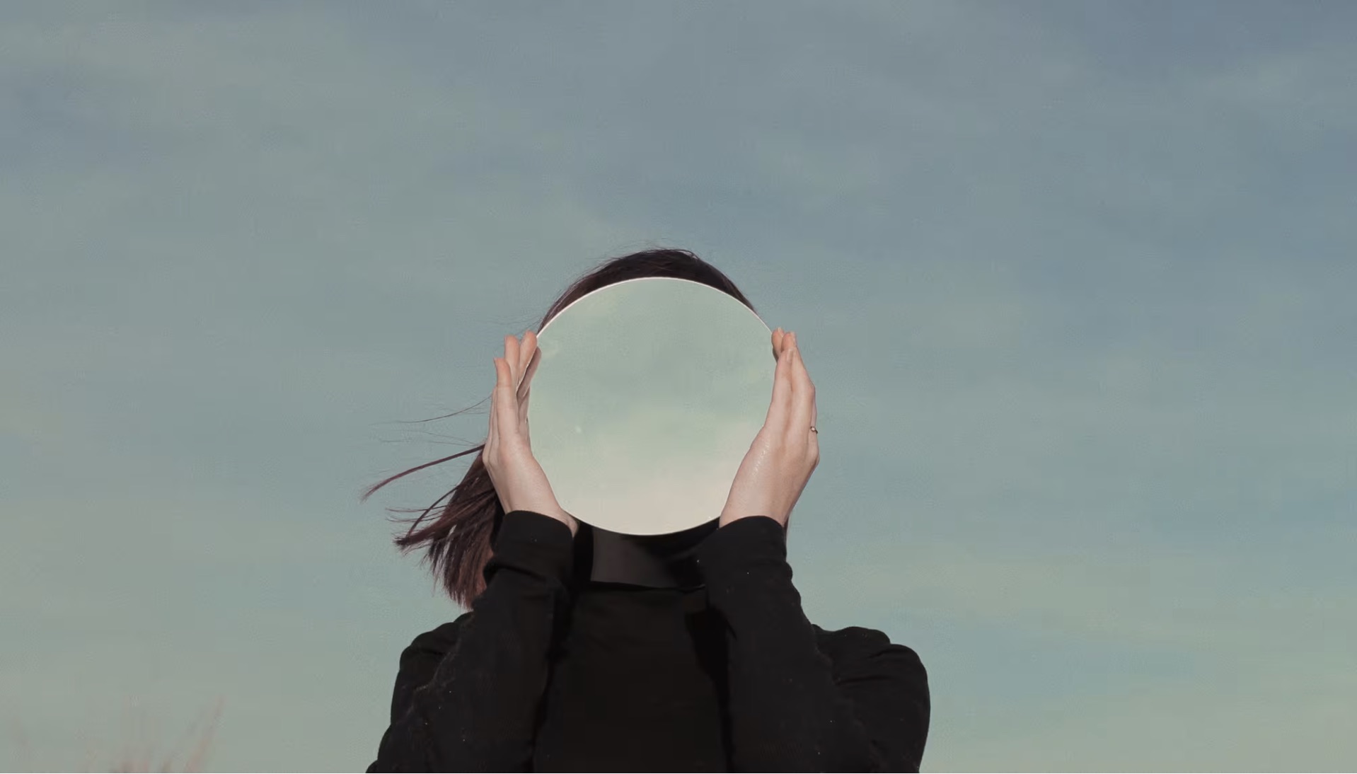 girl holding mirror in front of her face reflecting the sky