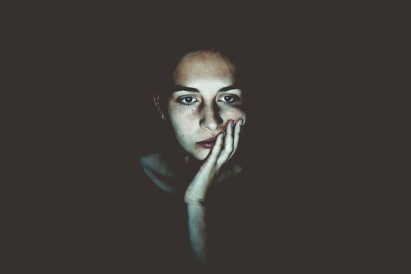 girl sitting alone in a dark room with only her face illuminated